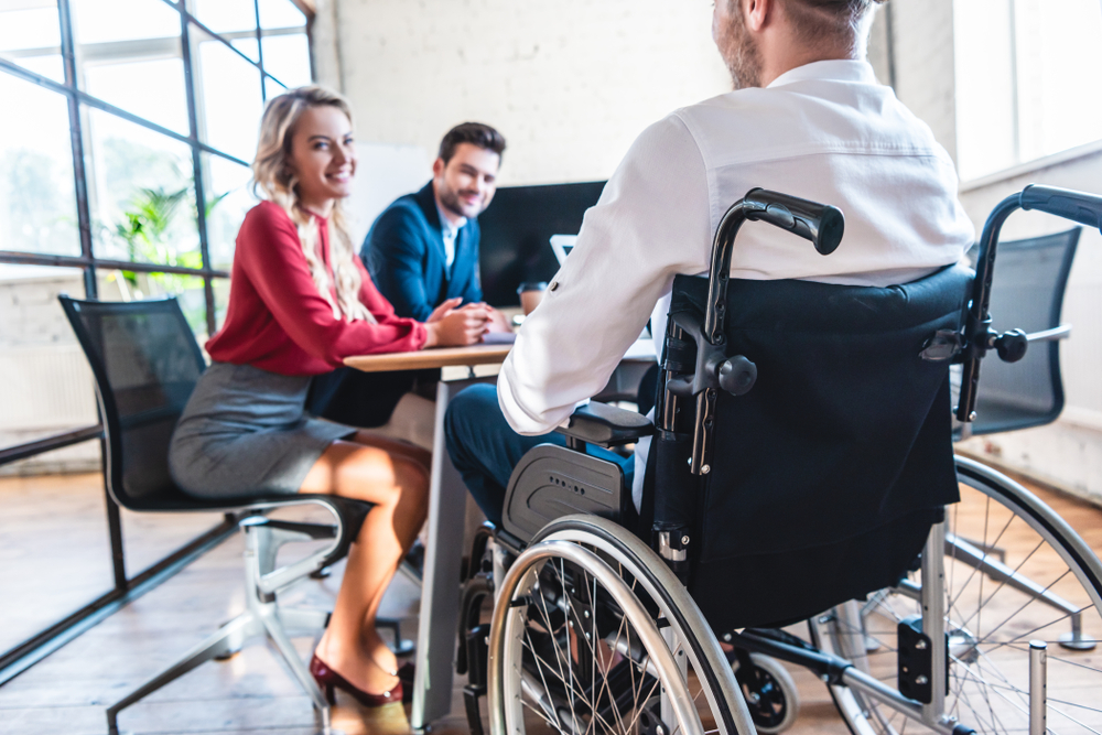 Partial,View,Of,Smiling,Businesspeople,Looking,At,Colleague,In,Wheelchair
